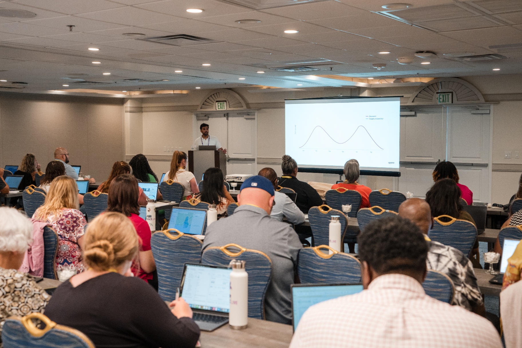Wide audience view of the speaker presenting a supply and demand chart