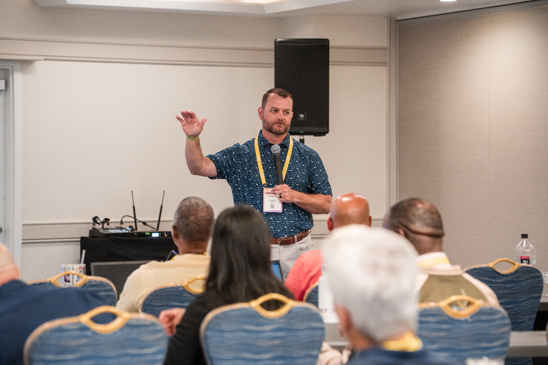 Audience view of a speaker in a patterned blue shirt leading a Day 2 presentation
