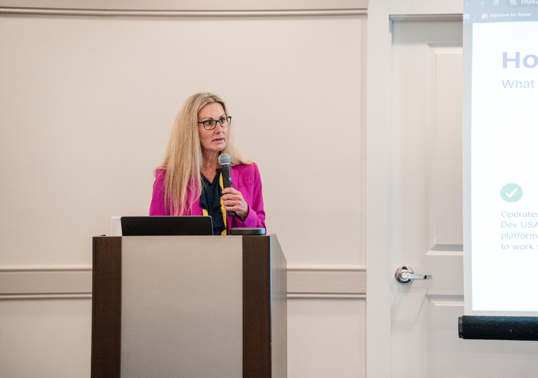 Speaker in pink blazer holding the microphone while presenting at the podium