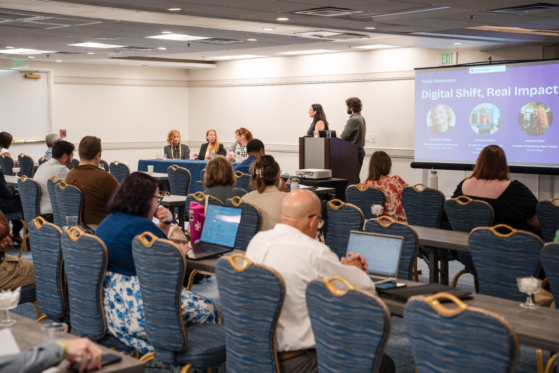 Panel discussion with three seated panelists and two presenters at the podium