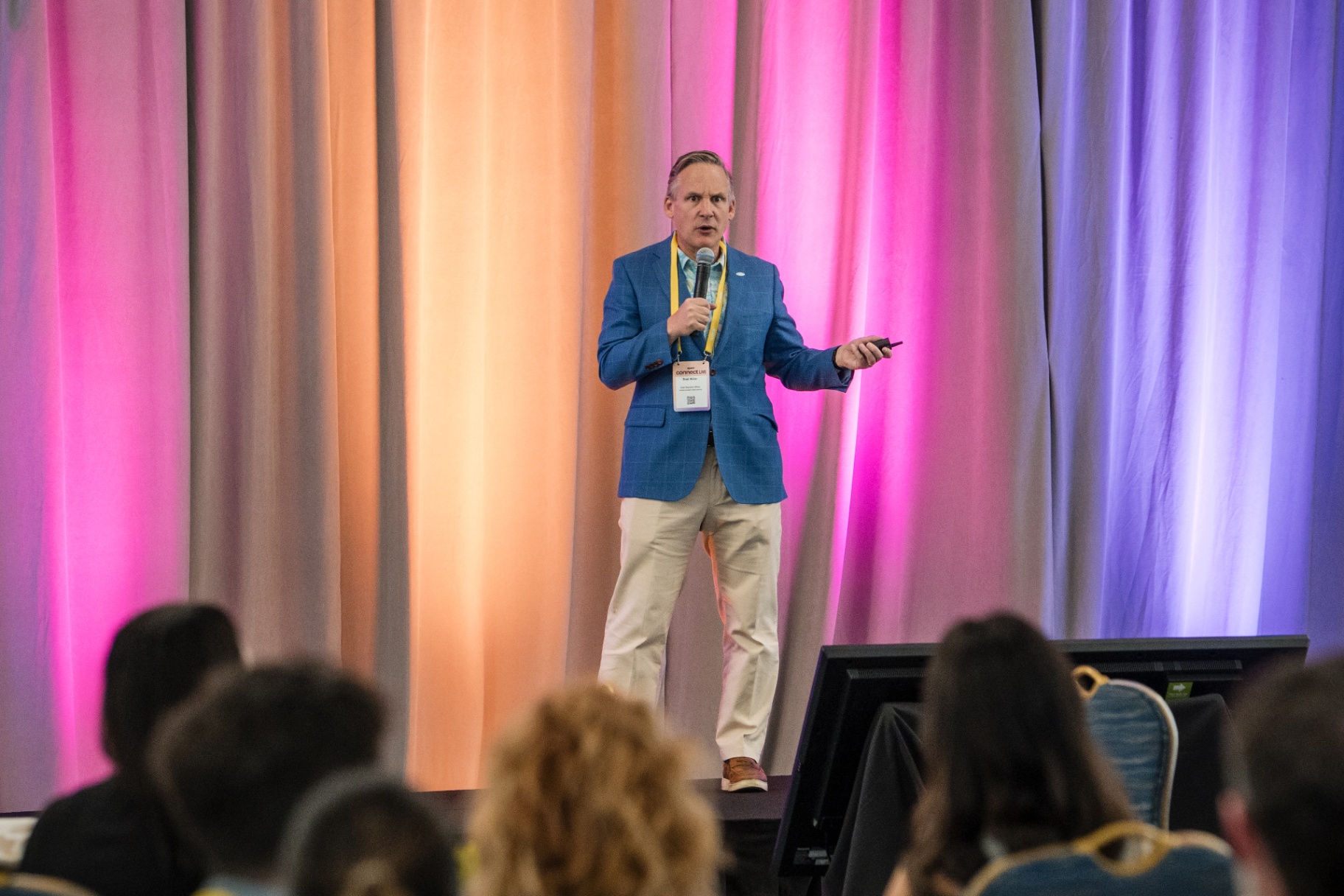Speaker presenting on stage with colorful drapery behind them