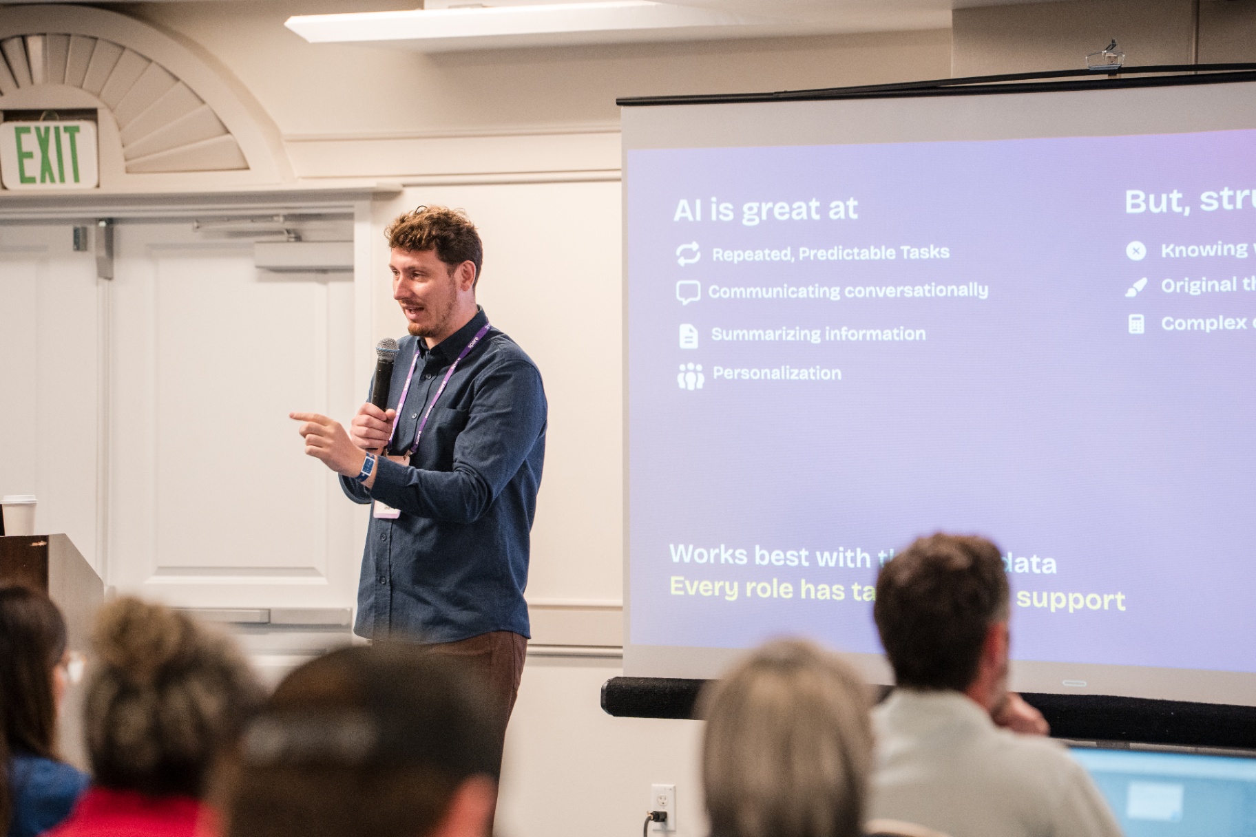 Presenter in a blue shirt beside the 'AI is great at' slide during the Day 2 AI session