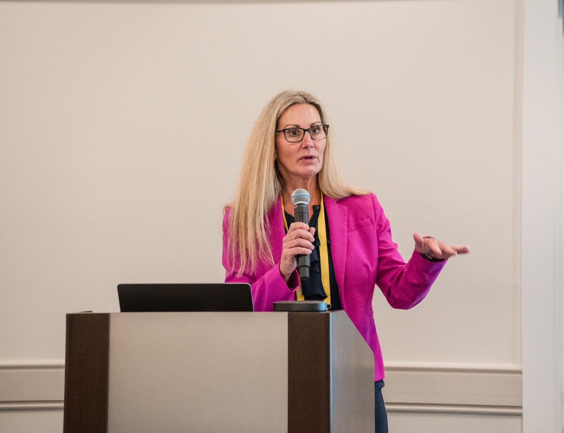 Close-up of a speaker in a bright pink blazer presenting from the podium