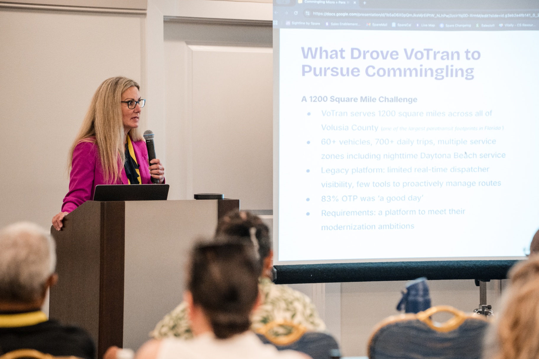 Close-up of the speaker at the podium beside the 'What Drove VoTran to Pursue Commingling' slide