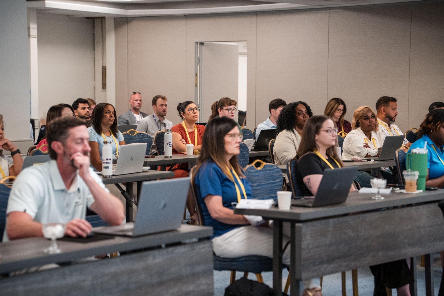 Engaged audience members seated at tables during the Day 2 session