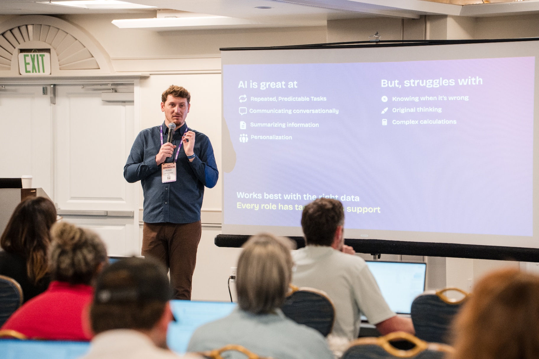 Wide view of the 'AI is great at / But, struggles with' slide and the presenter on stage