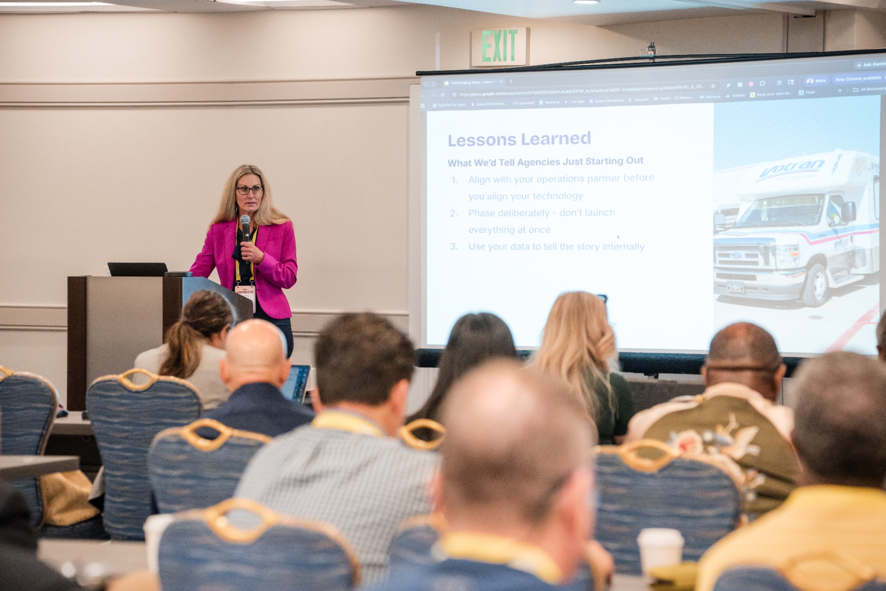 Speaker in pink blazer beside the 'Lessons Learned' slide with a VoTran vehicle image